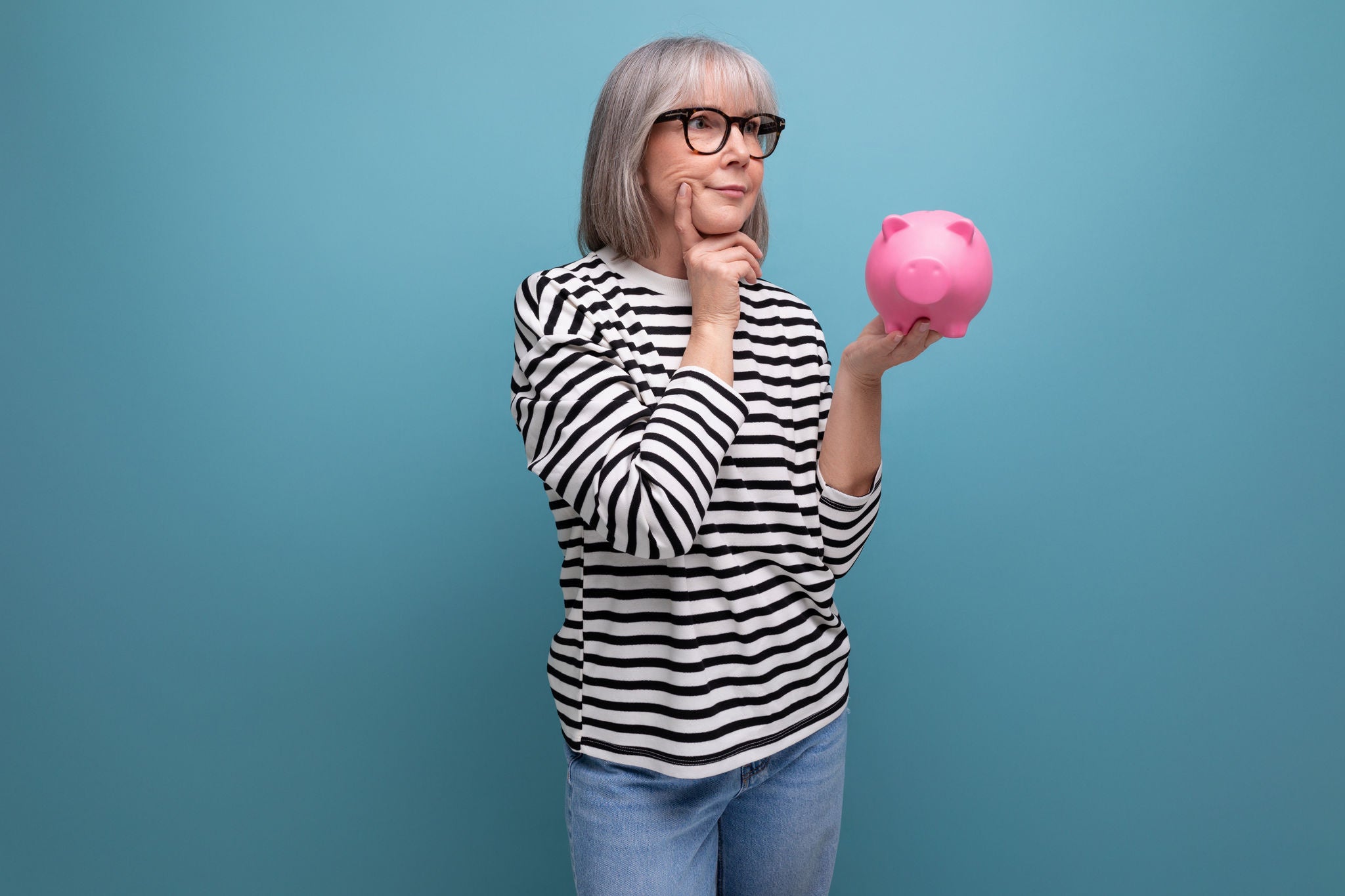 ingenious grandmother middle-aged woman has an idea where to invest her savings from a piggy bank on a bright background with save space.