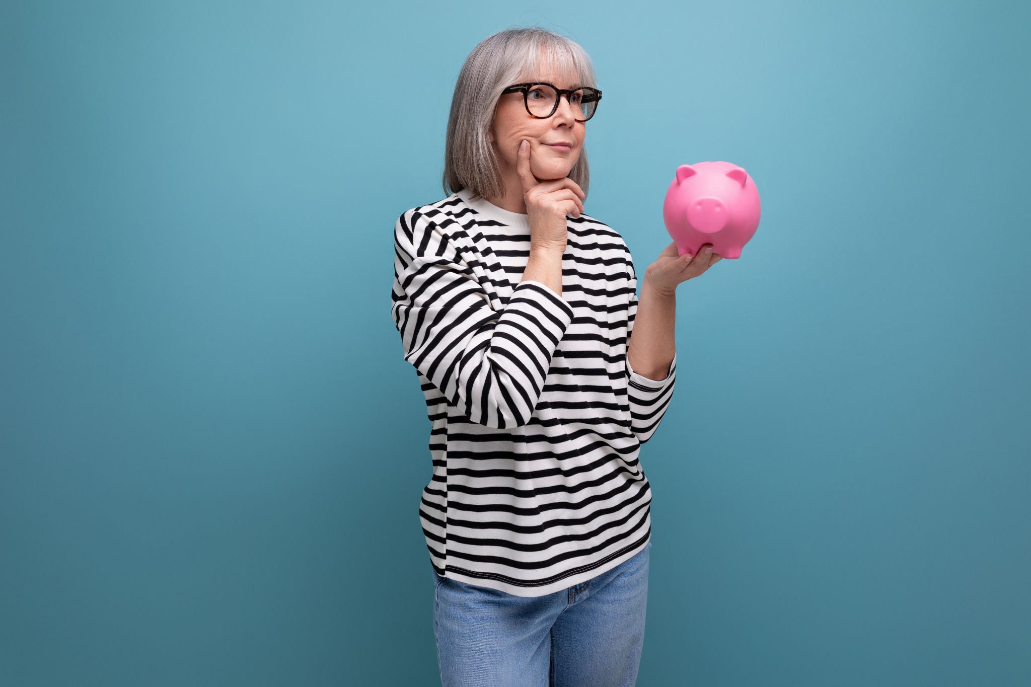 ingenious grandmother middle-aged woman has an idea where to invest her savings from a piggy bank on a bright background with save space, ingenious grandmother middle-aged woman has an idea where to inv